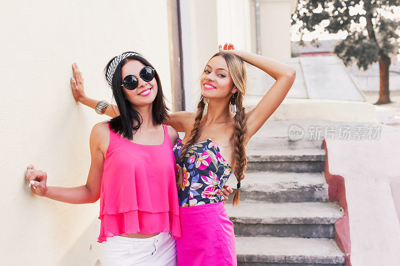 Two pretty sisters hipster girls hugging and having fun together on the background of graffiti wearing bright fashionable clothes and big glasses, positive emotions, bright colors